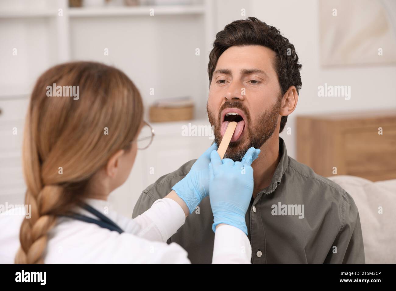 Doctor examining man`s oral cavity with tongue depressor indoors Stock